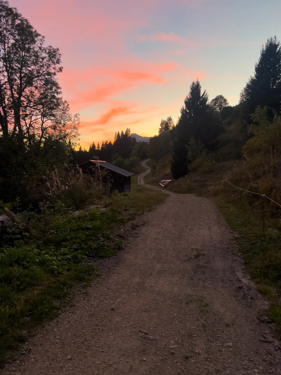 Gravel track and wooden barn under a pink sunset sky near Les Gets