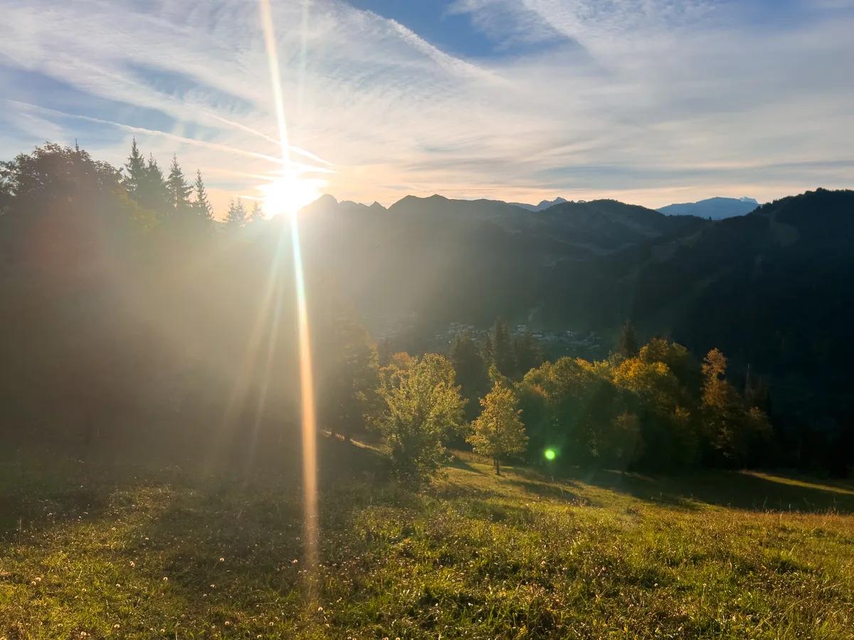 Soleil du matin se levant sur les montagnes au-dessus des Gets, arbres d'automne et prairie au premier plan