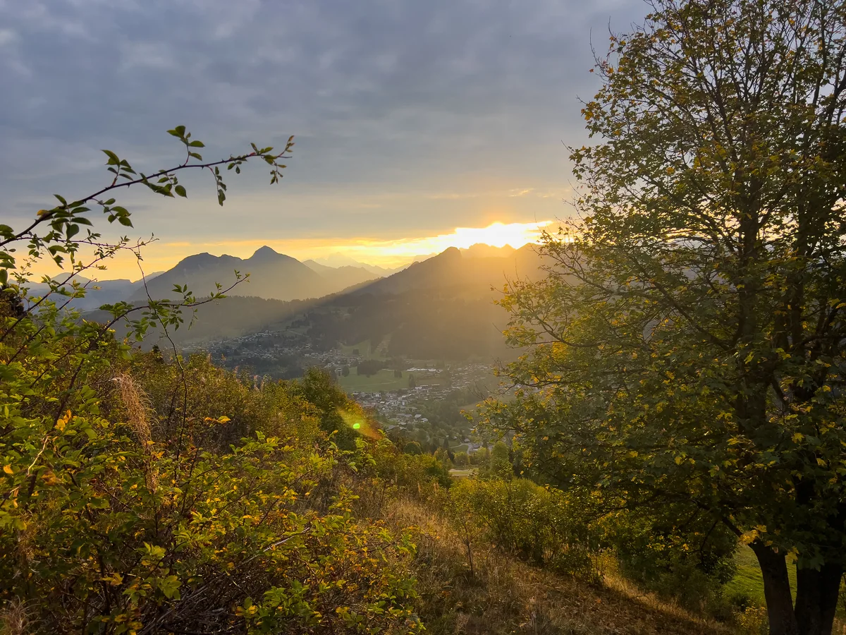 Le soleil du matin perçant au-dessus d'une crête, les feuilles d'automne encadrant le village en contrebas.