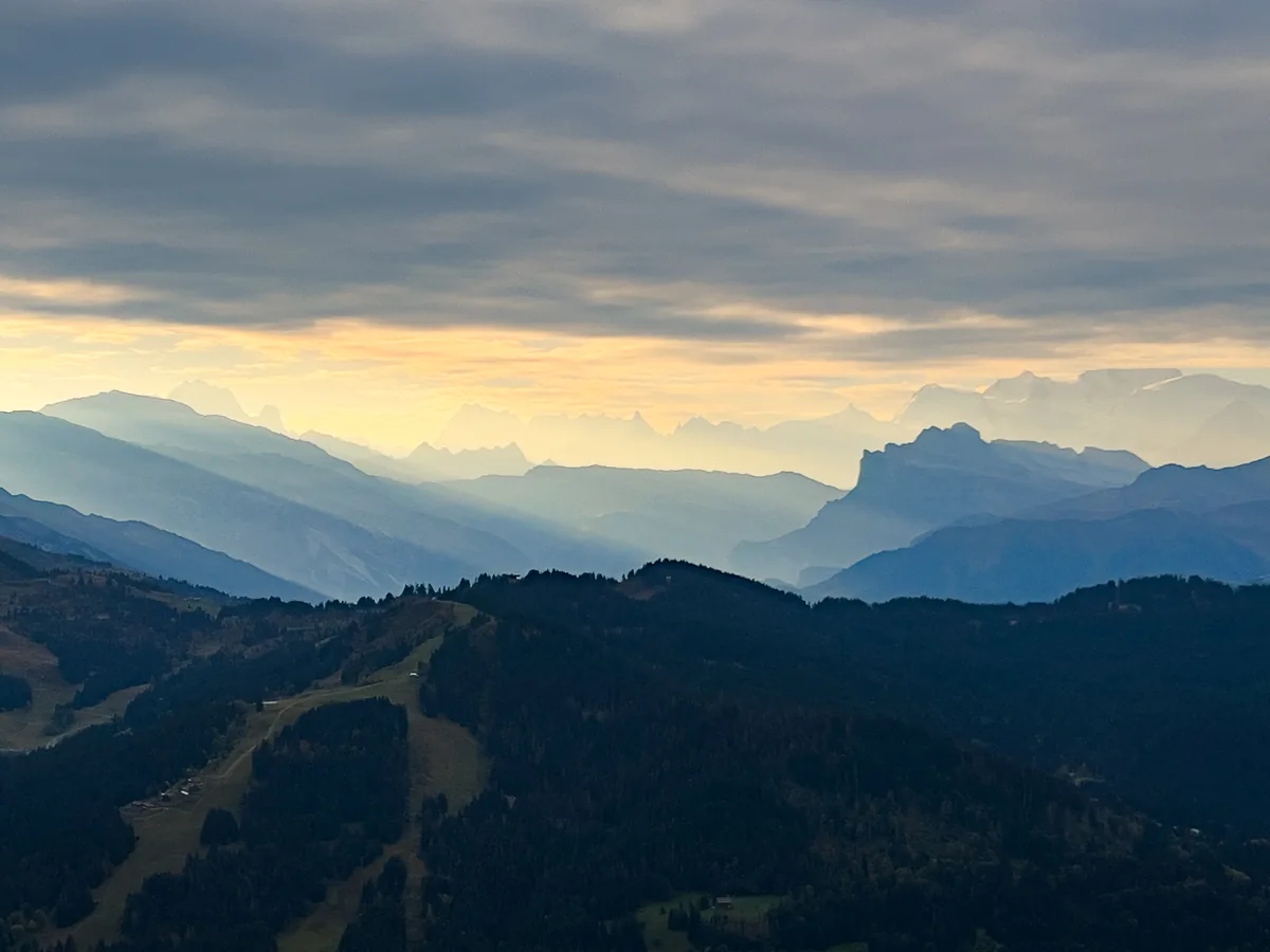 Des crêtes de montagnes bleutées en couches sous les nuages gris et un ciel doré.